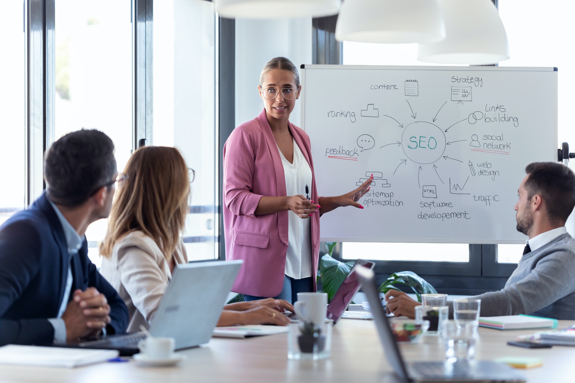 young businesswoman pointing at white blackboard and explain a project to her colleagues